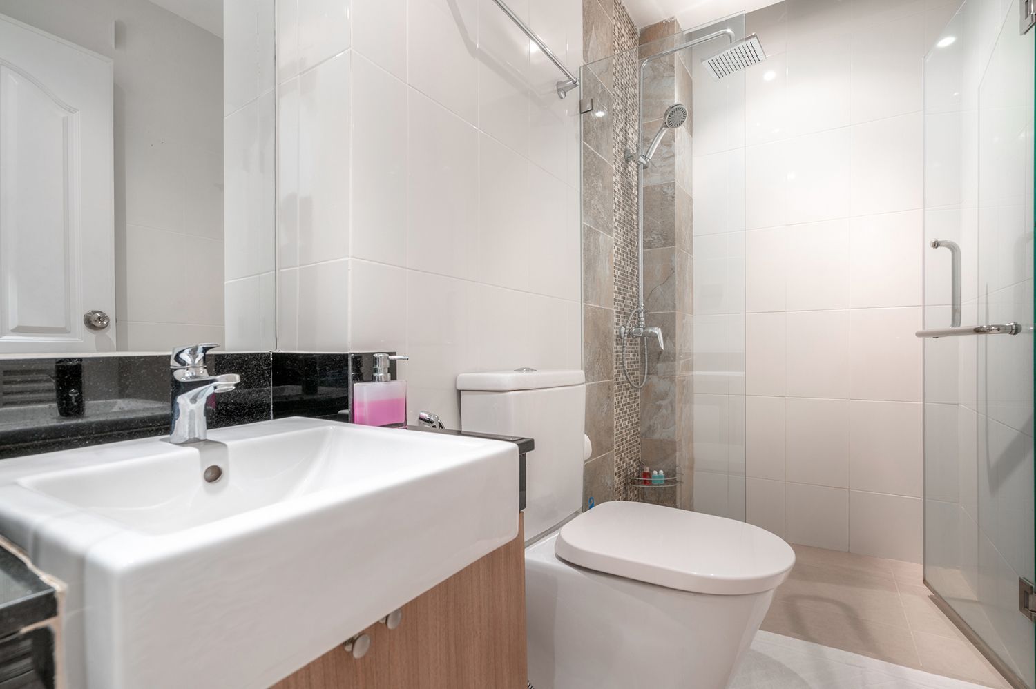 A modern bathroom with a white sink, toilet, shower, and tiled walls.