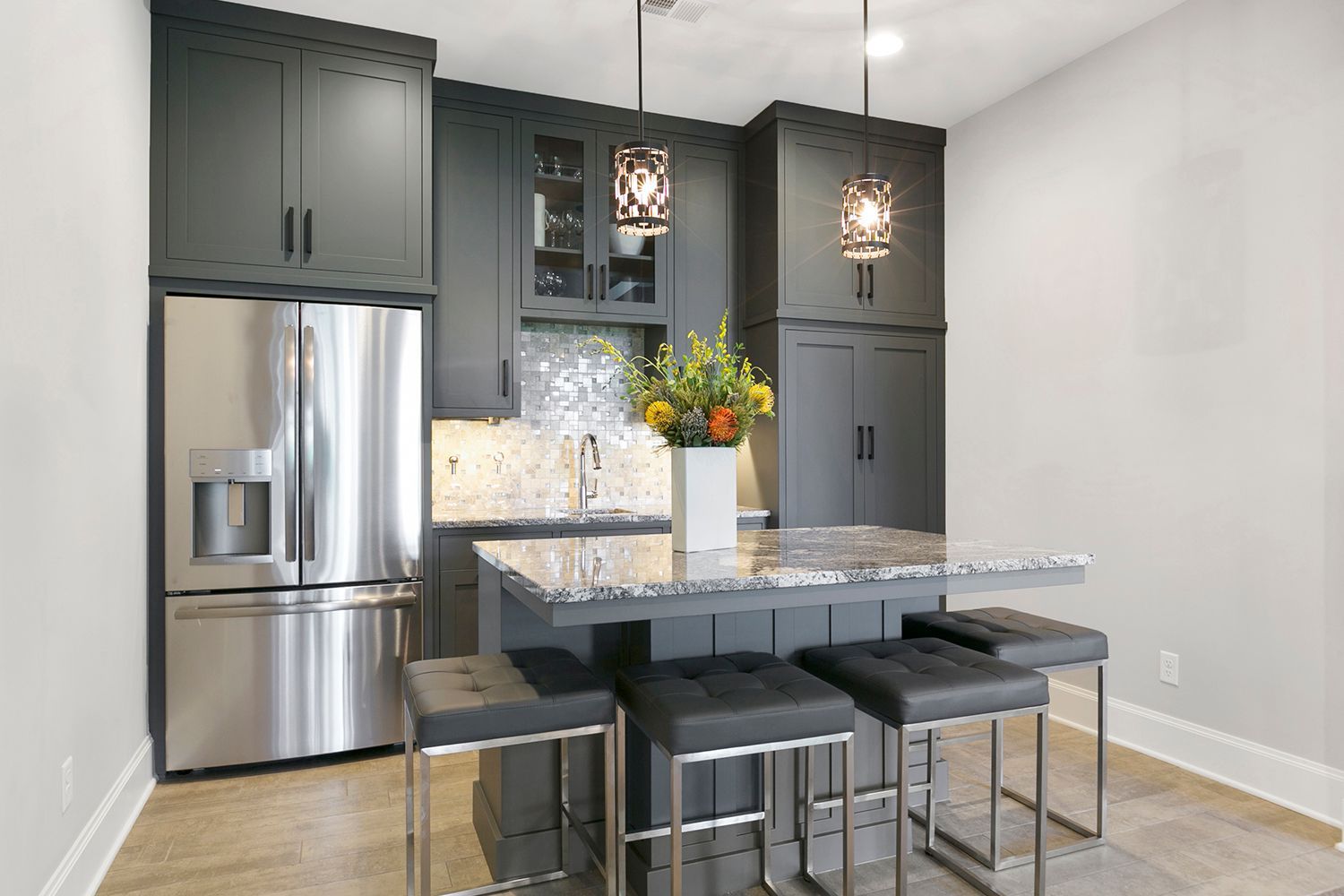 Dark gray kitchen with stainless steel refrigerator, island, and three stools.