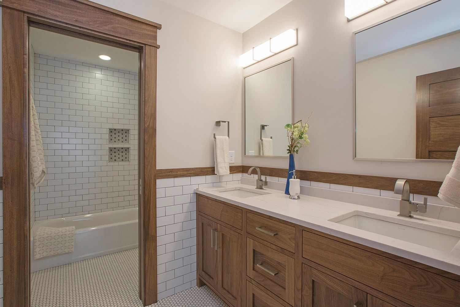 Bathroom with wood vanity, white countertops, and a doorway to a tiled tub area. Bathroom with wood vanity, white countertops, and a doorway to a tiled tub area.