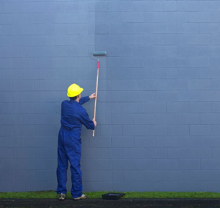 Person painting a blue wall with a roller, wearing a yellow hard hat and blue jumpsuit. Person painting a blue wall with a roller, wearing a yellow hard hat and blue jumpsuit.