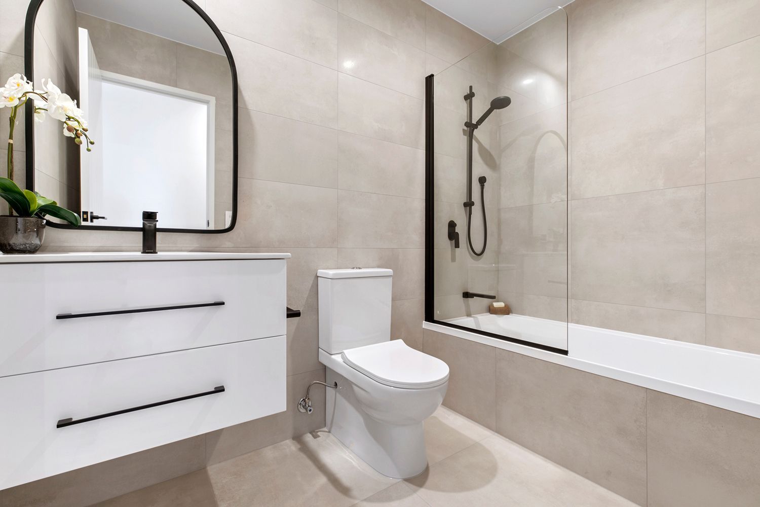 Modern bathroom with a white vanity, toilet, and bathtub; neutral tiles. Modern bathroom with a white vanity, toilet, and bathtub; neutral tiles.