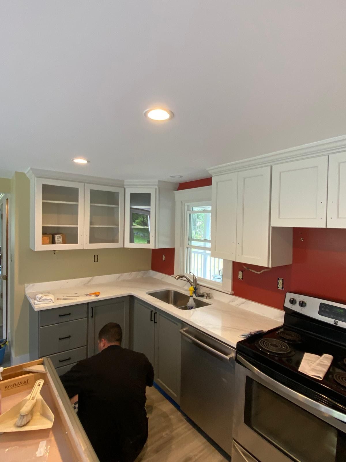 A person works on a newly renovated kitchen with grey and white cabinets, red backsplash, and a stainless steel stove. A person works on a newly renovated kitchen with grey and white cabinets, red backsplash, and a stainless steel stove.
