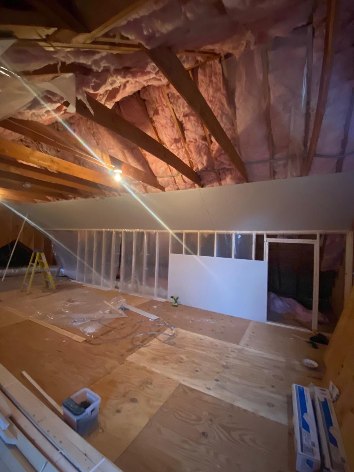 Attic renovation in progress: framing, insulation, plywood flooring, unfinished walls, and exposed beams.