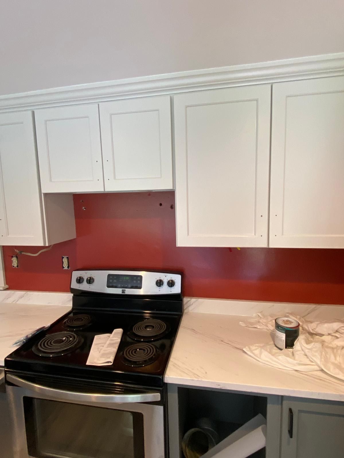 Kitchen with white cabinets, red backsplash, black stove, and gray countertops. Kitchen with white cabinets, red backsplash, black stove, and gray countertops.