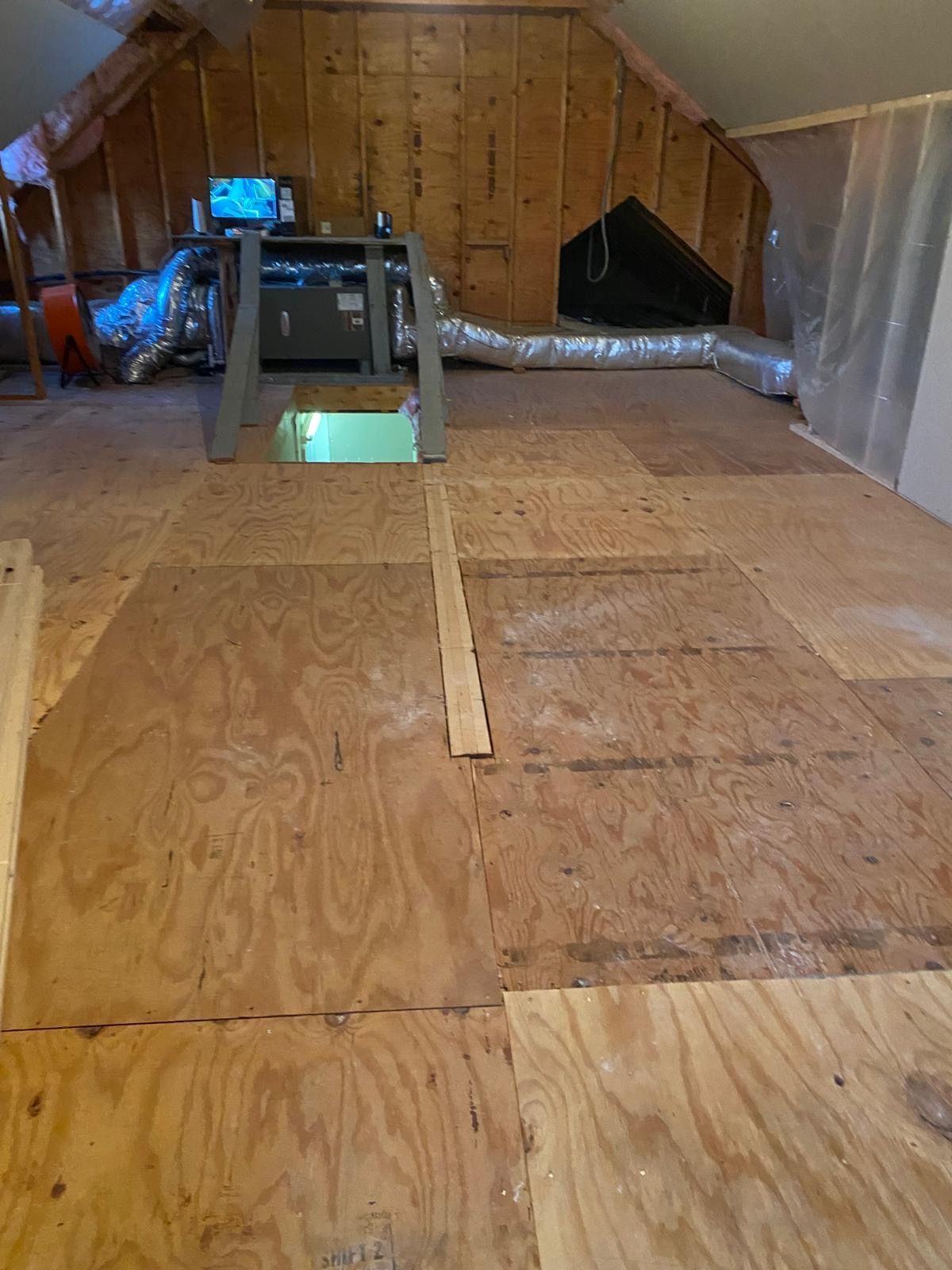 Attic with plywood flooring, a HVAC system, and an access hatch.
