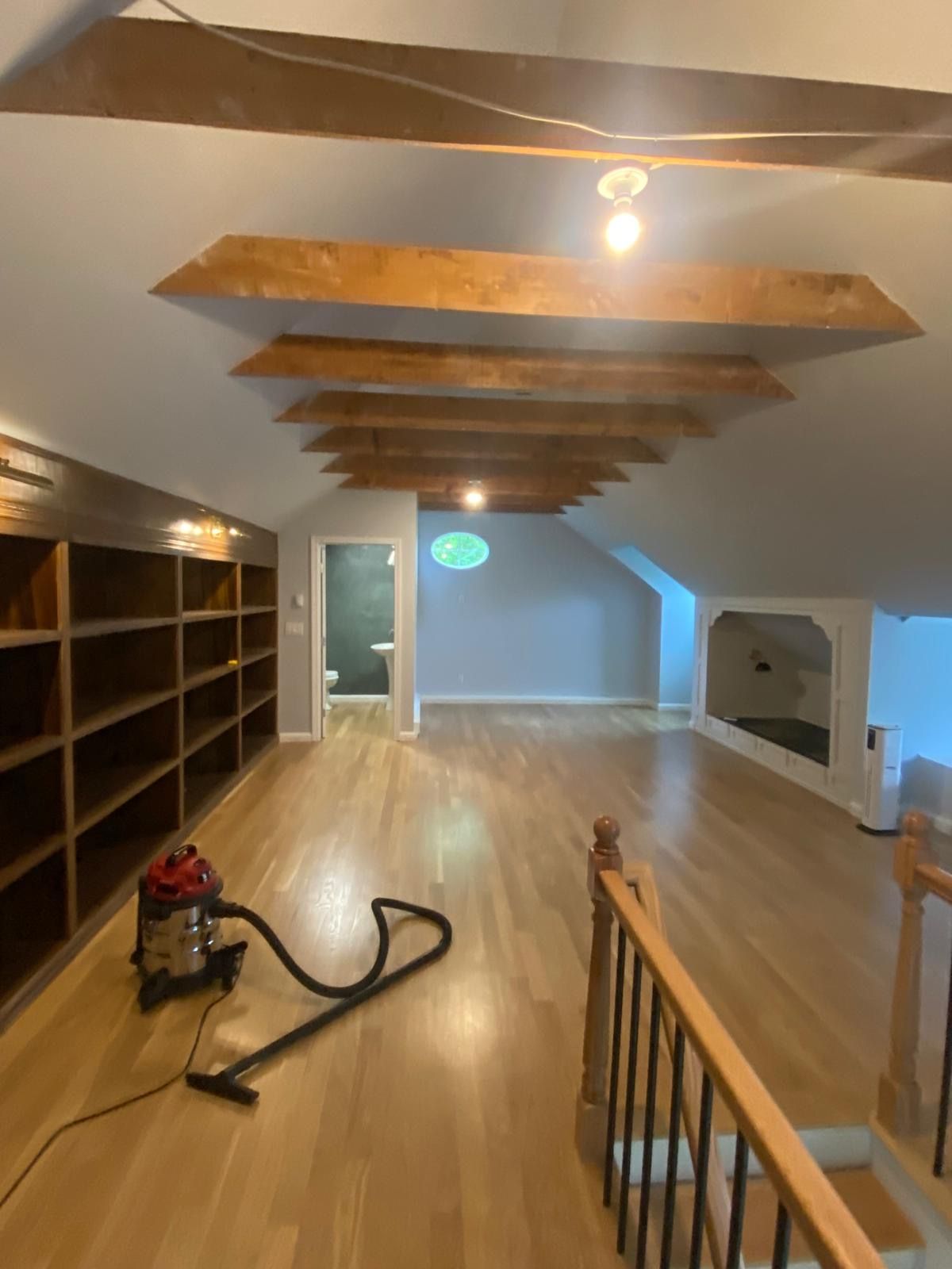 Loft room with wood beams, built-in shelves, hardwood floor, and a vacuum. Loft room with wood beams, built-in shelves, hardwood floor, and a vacuum.