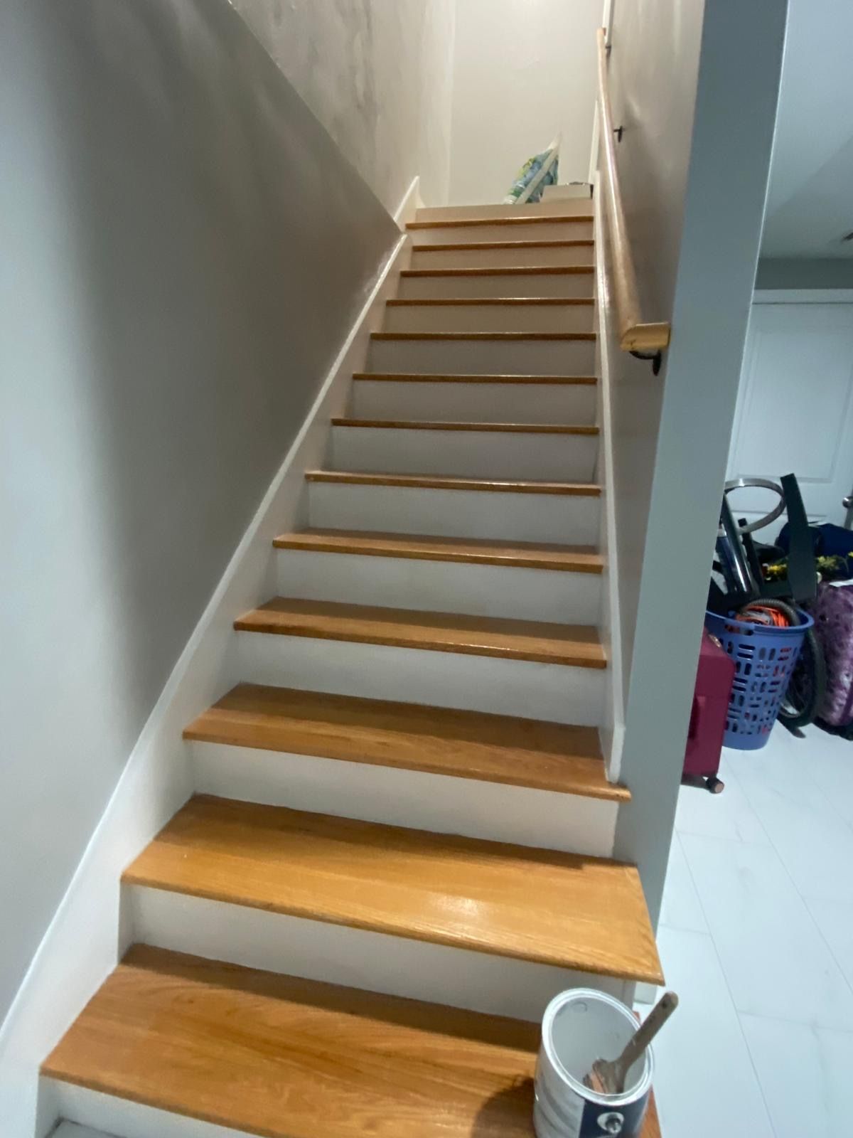 Wooden staircase with white risers, painted gray walls, and a bucket on a step. Wooden staircase with white risers, painted gray walls, and a bucket on a step.