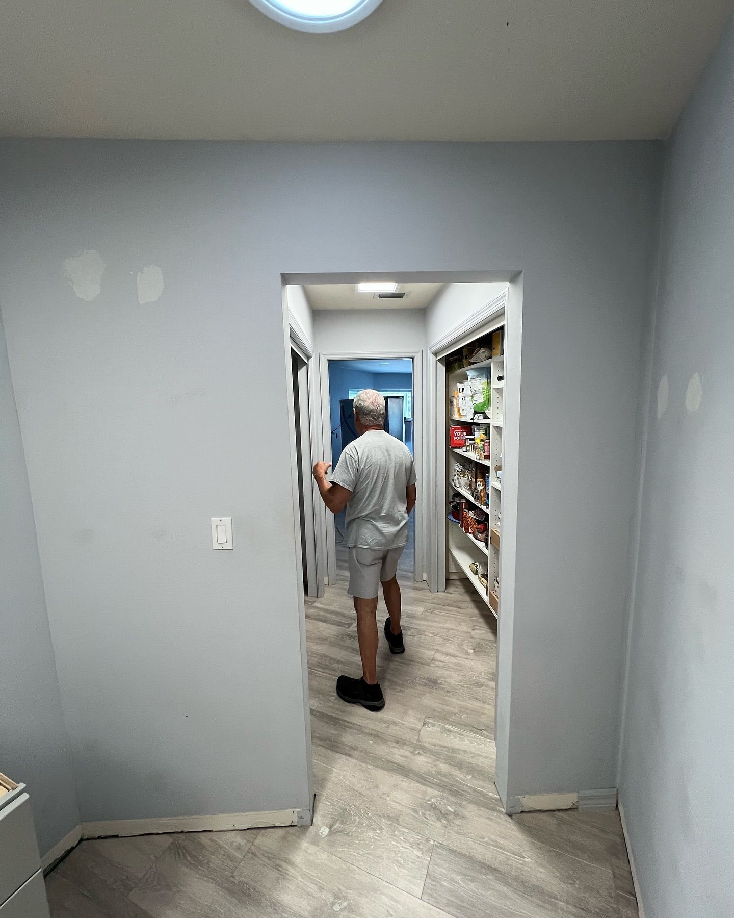 A man is standing in a hallway looking into a pantry.