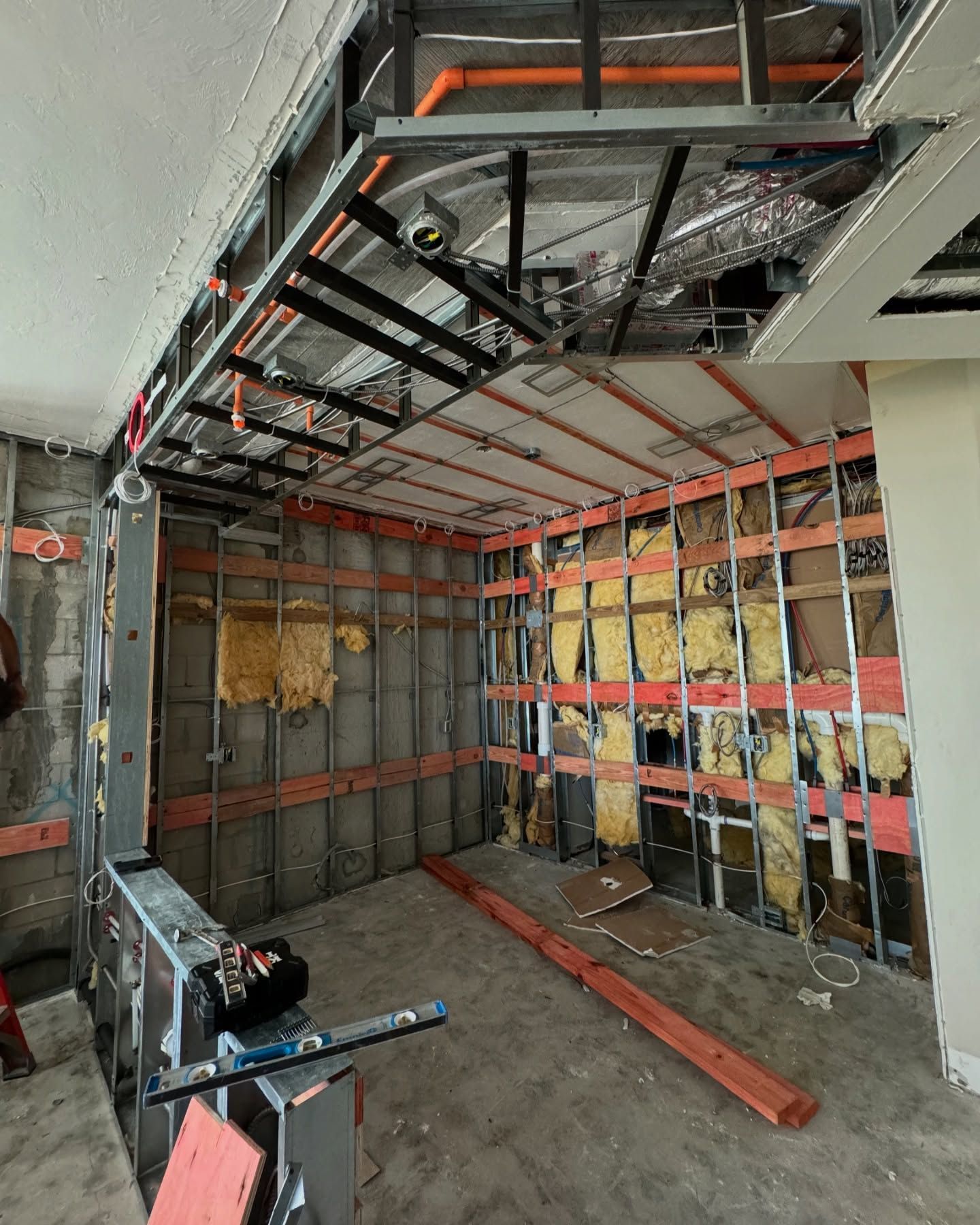 A room that is being remodeled with a lot of pipes hanging from the ceiling.