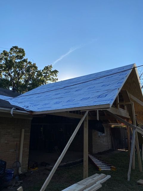 Partially roofed house with shiny metal sheeting and support beams under a blue sky