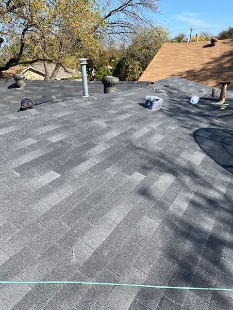 New gray roof shingles being installed, with vents and tools visible on a residential rooftop.