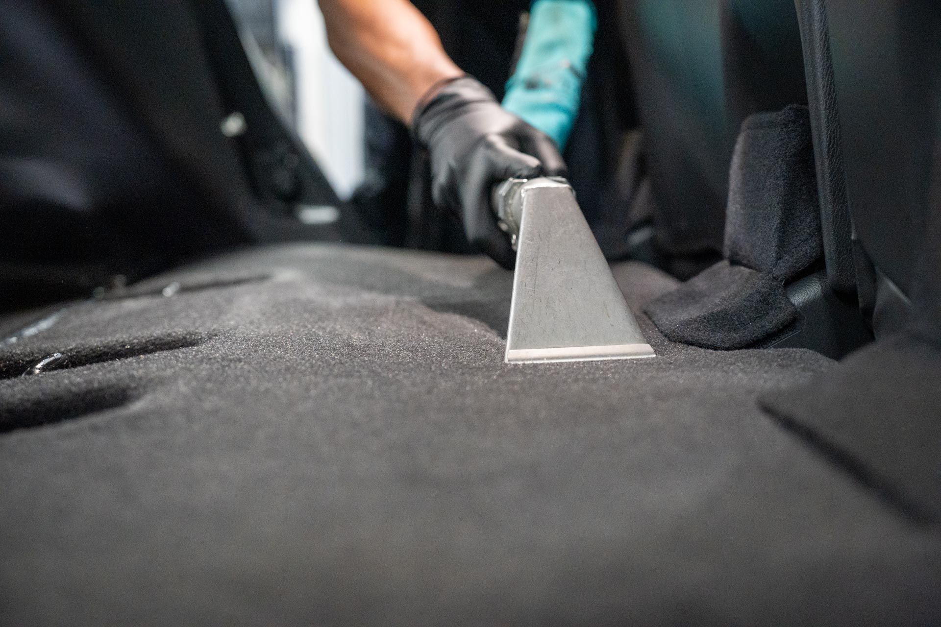 A person is cleaning the back seat of a car with a vacuum cleaner.