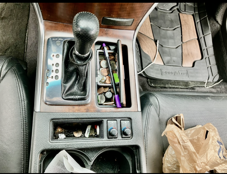 The center console of a car with a pen and coins in it