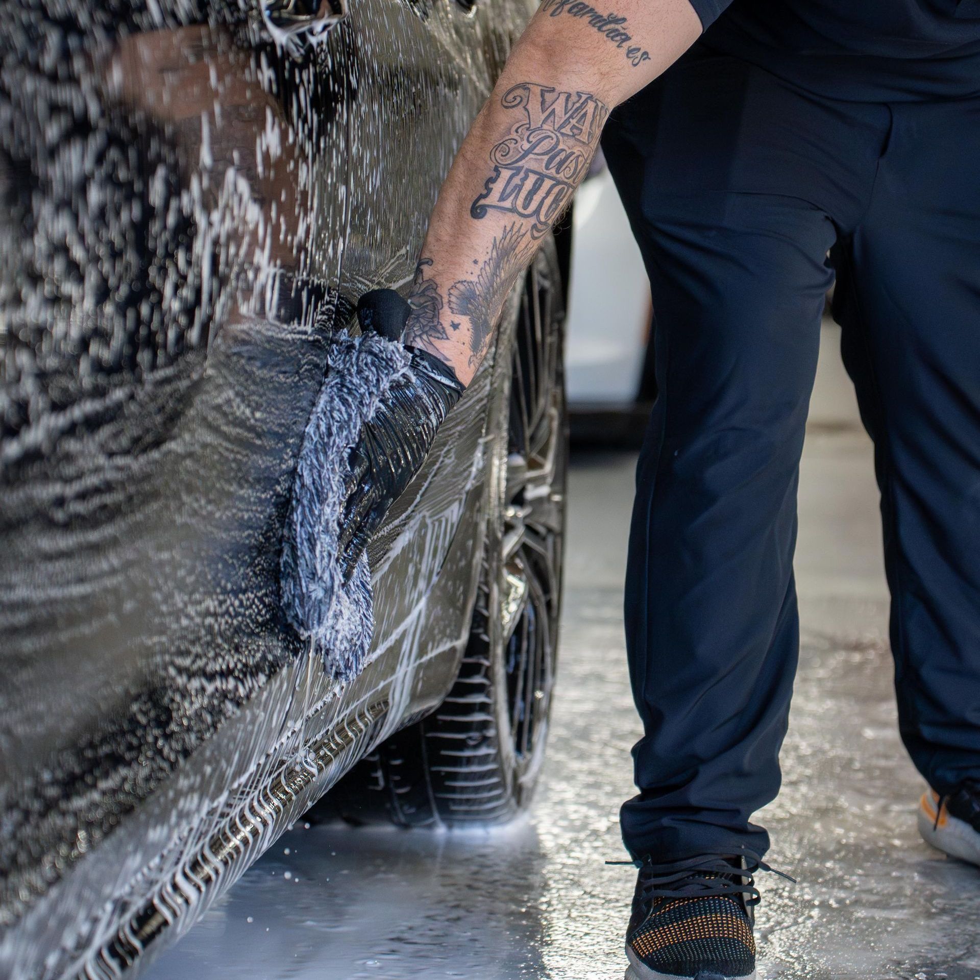 A man with a tattoo on his arm is washing a car