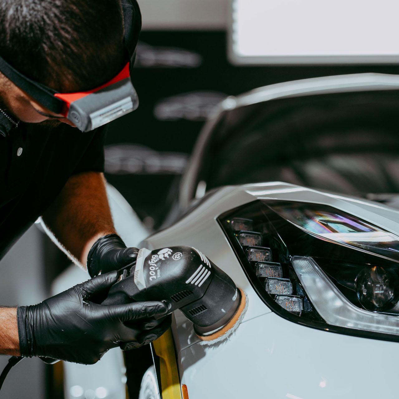 A man wearing goggles is polishing a car with a machine