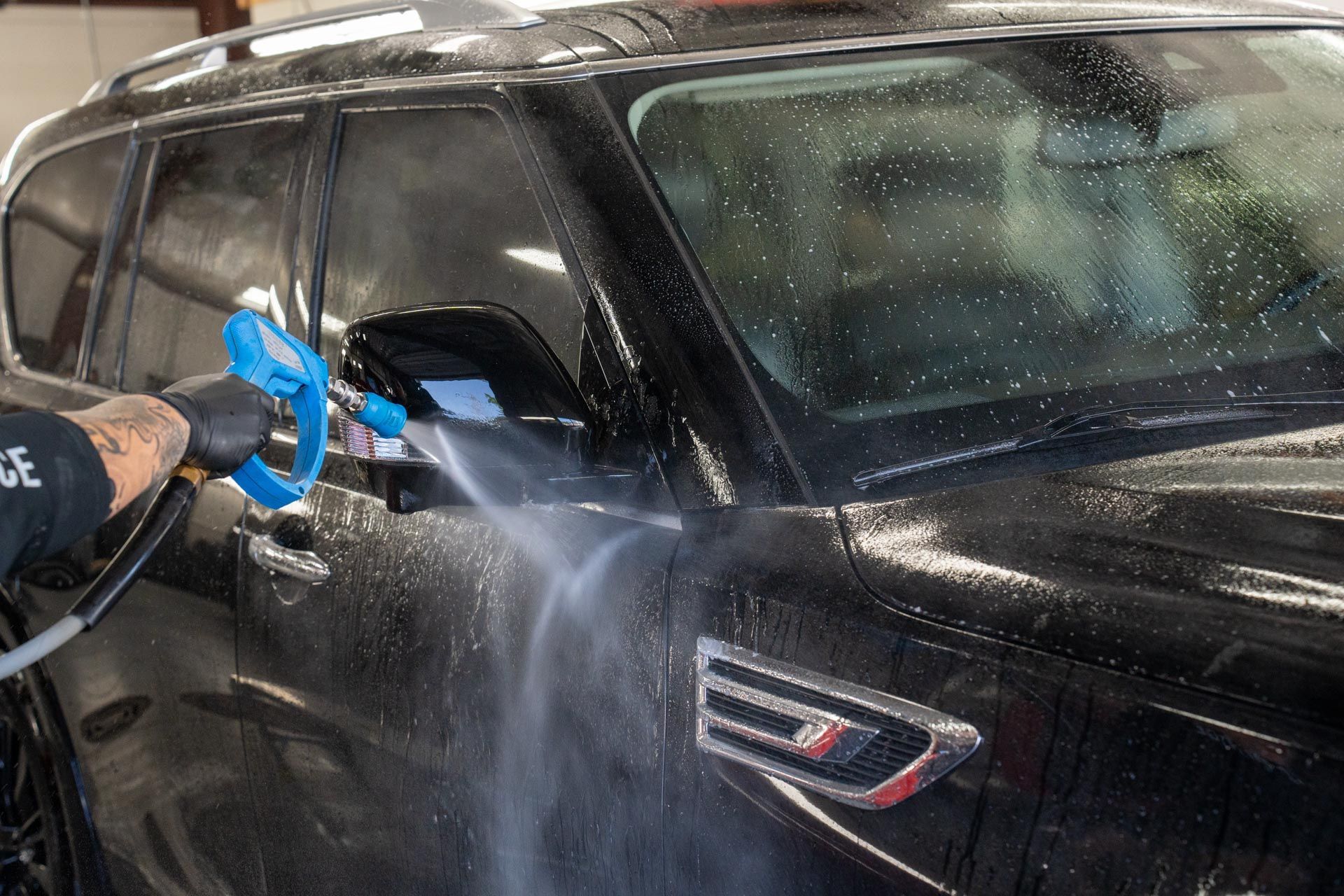 A man is washing a black car with a hose.