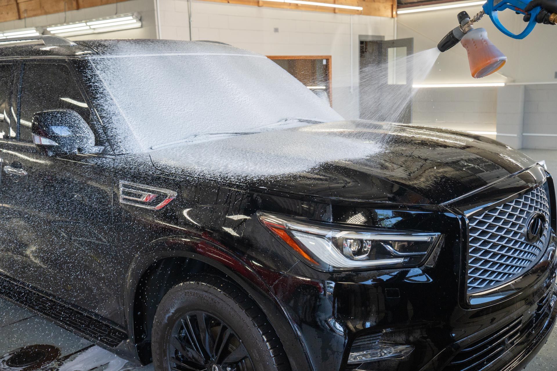 A black suv is being washed with foam in a garage.