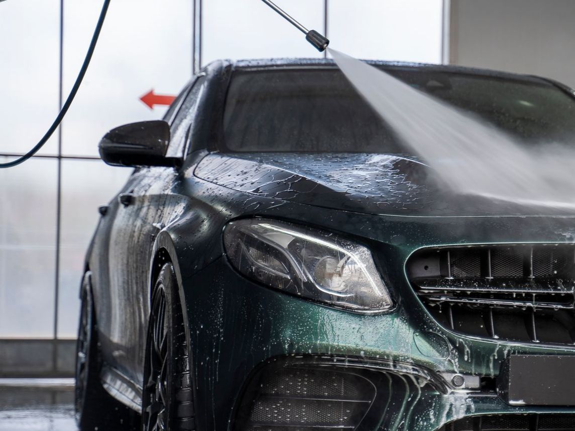 A man is washing a black car with a hose.