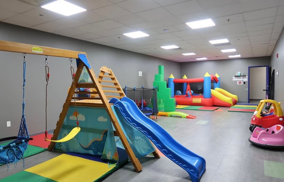 Indoor children's play area with swings, slide, inflatable bounce houses, and ride-on toys.