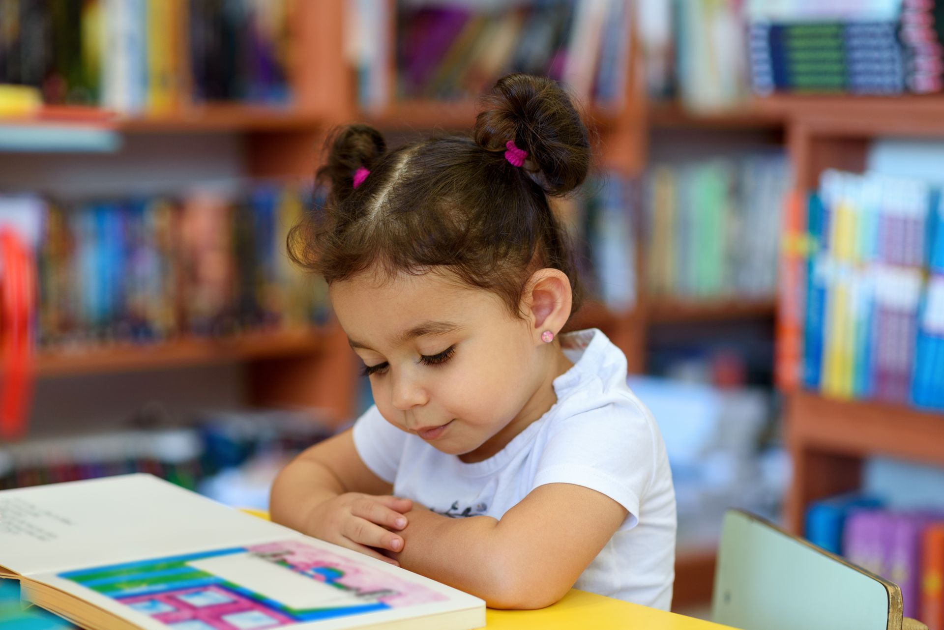 Young child reading a book in a library, with a focused expression.