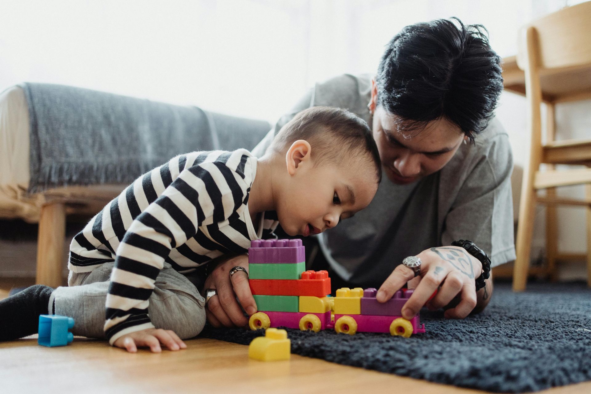 Father and child building a toy train together on a rug.
