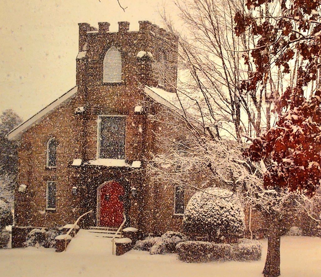 Stone church building with a sign and flowers in the yard.