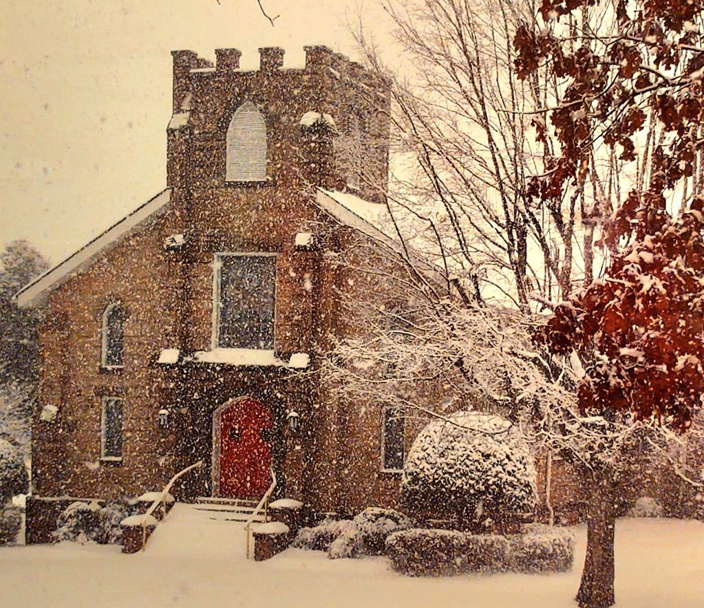Stone church with red door in a snowy setting.