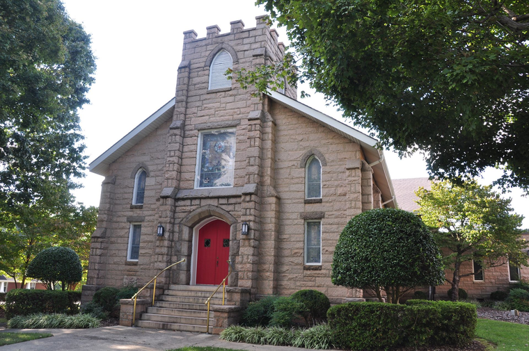 Stone church building with a sign and flowers in the yard.