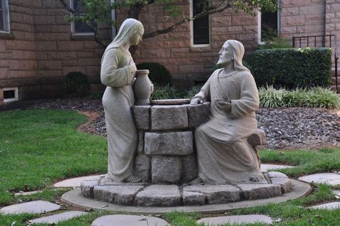 Statue of Jesus speaking with a woman at a well. They are in a garden setting.