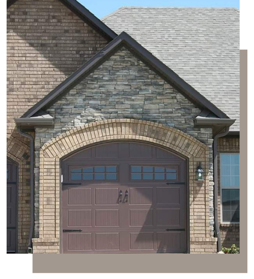 A brown garage door with windows, set in a stone and brick archway under a peaked roof on a residential house.