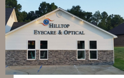 Exterior view of Hilltop Eyecare & Optical, a white building with stone siding and a parking lot.