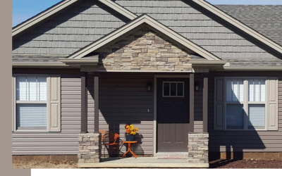 A suburban house entrance with tan siding, stone accents, a dark front door, and a small porch with seating.