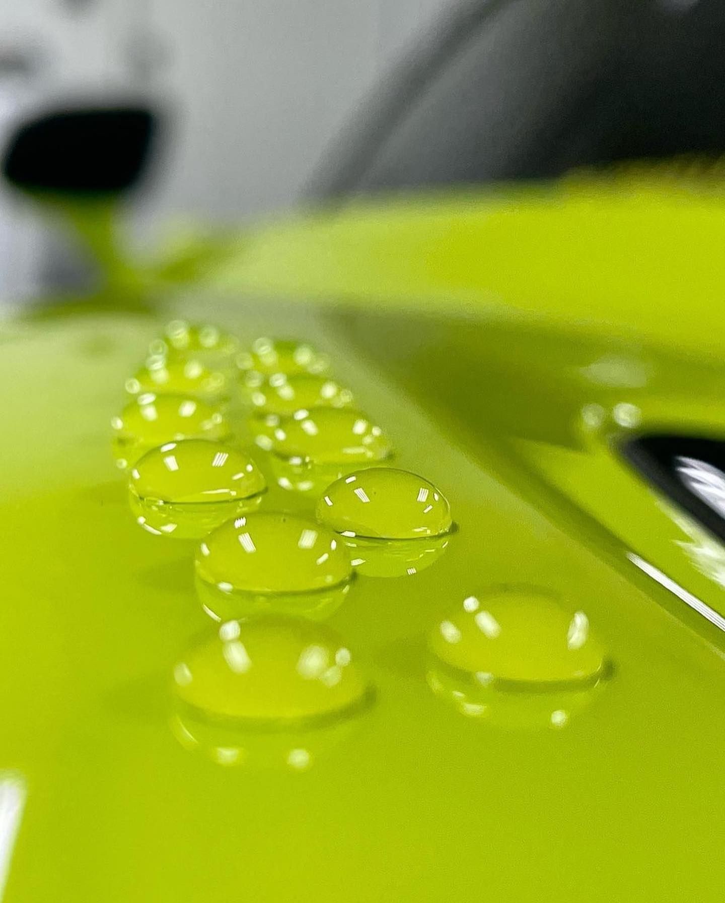 Close-up of water beads on a bright, lime-green car surface.