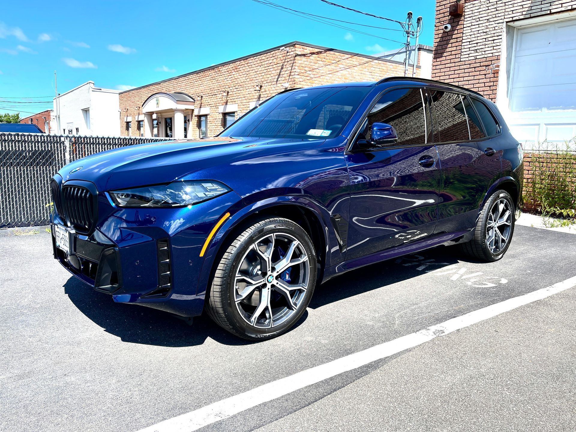 A blue bmw x5 is parked in a parking lot in front of a brick building.