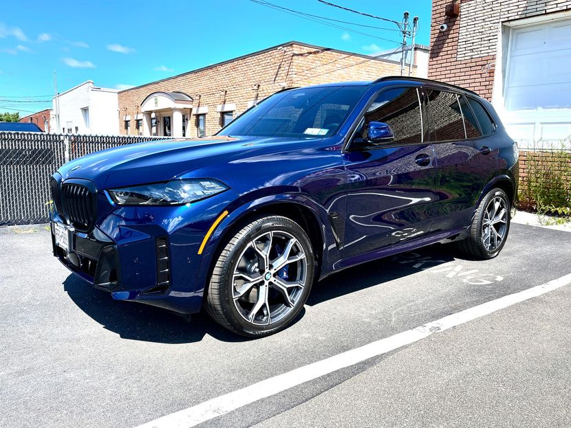 A blue bmw x5 is parked in a parking lot in front of a brick building.