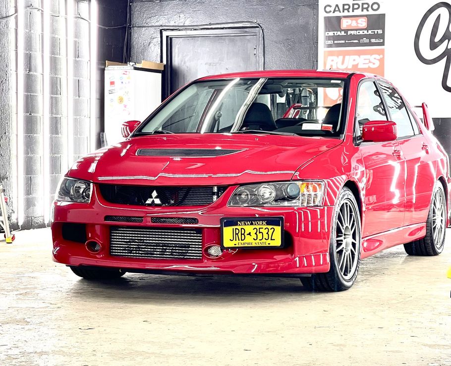 A red car with a yellow license plate is parked in a garage.