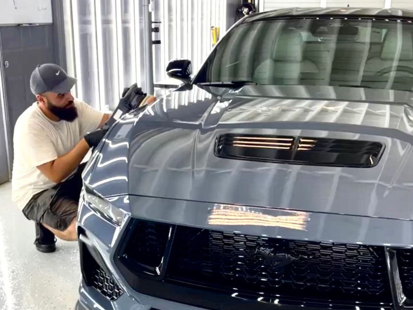 A man is cleaning the hood of a gray mustang in a garage.