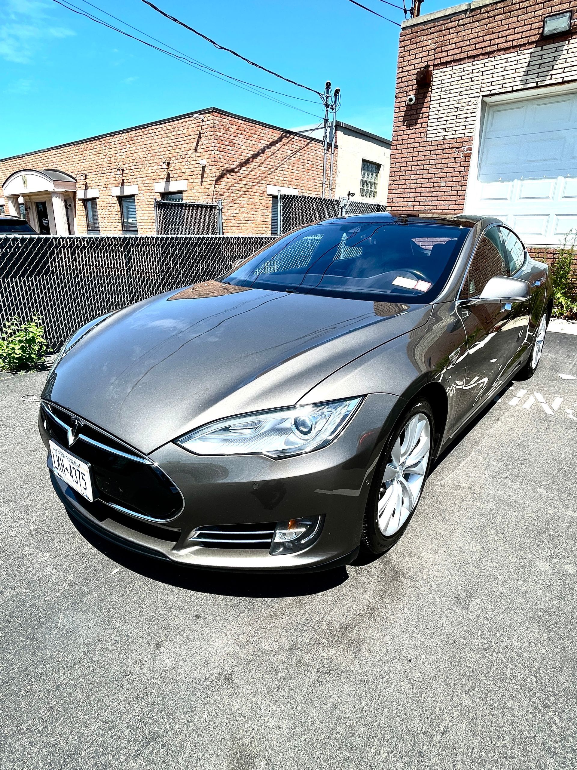 A gray tesla model s is parked in a driveway in front of a house.