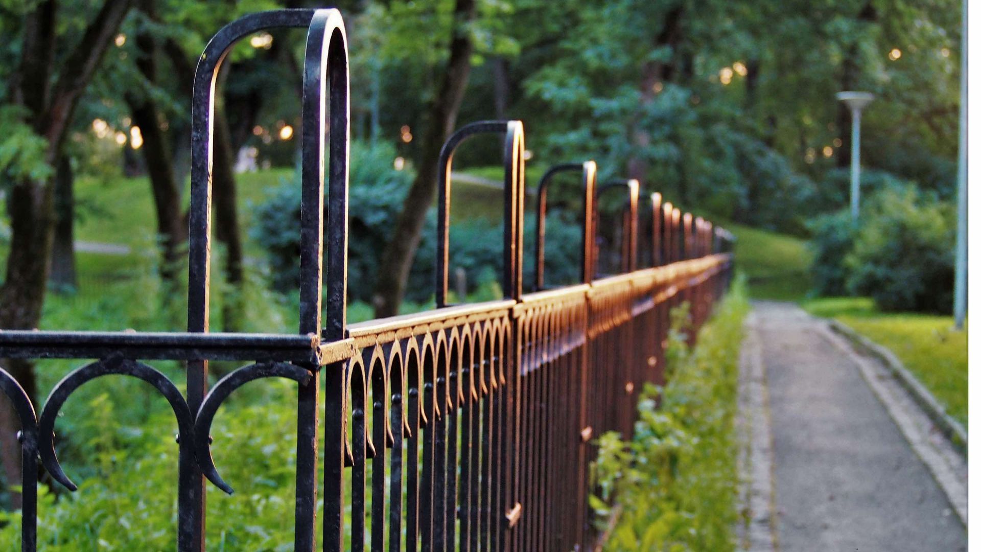 A wrought iron fence surrounds a path in a park.