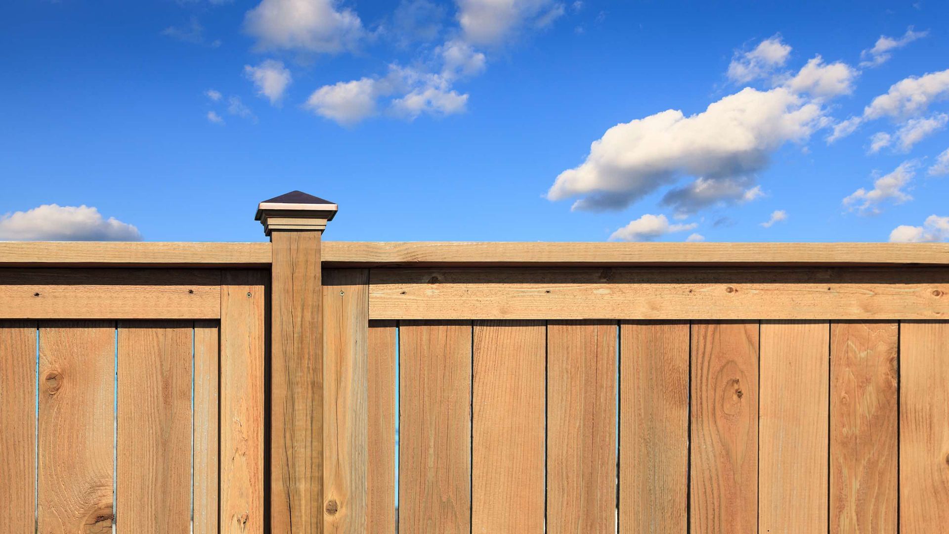A wooden fence with a blue sky and clouds in the background.
