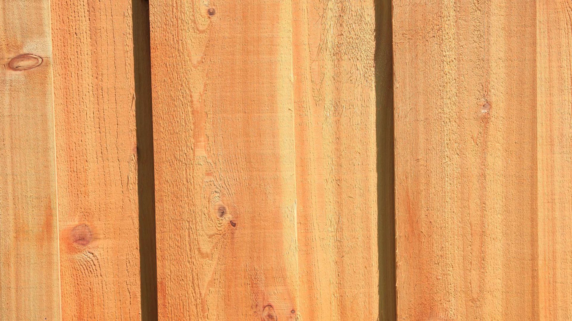 Close-up of vertical wooden planks, showing wood grain. Brown and orange hues with shadows between the planks.