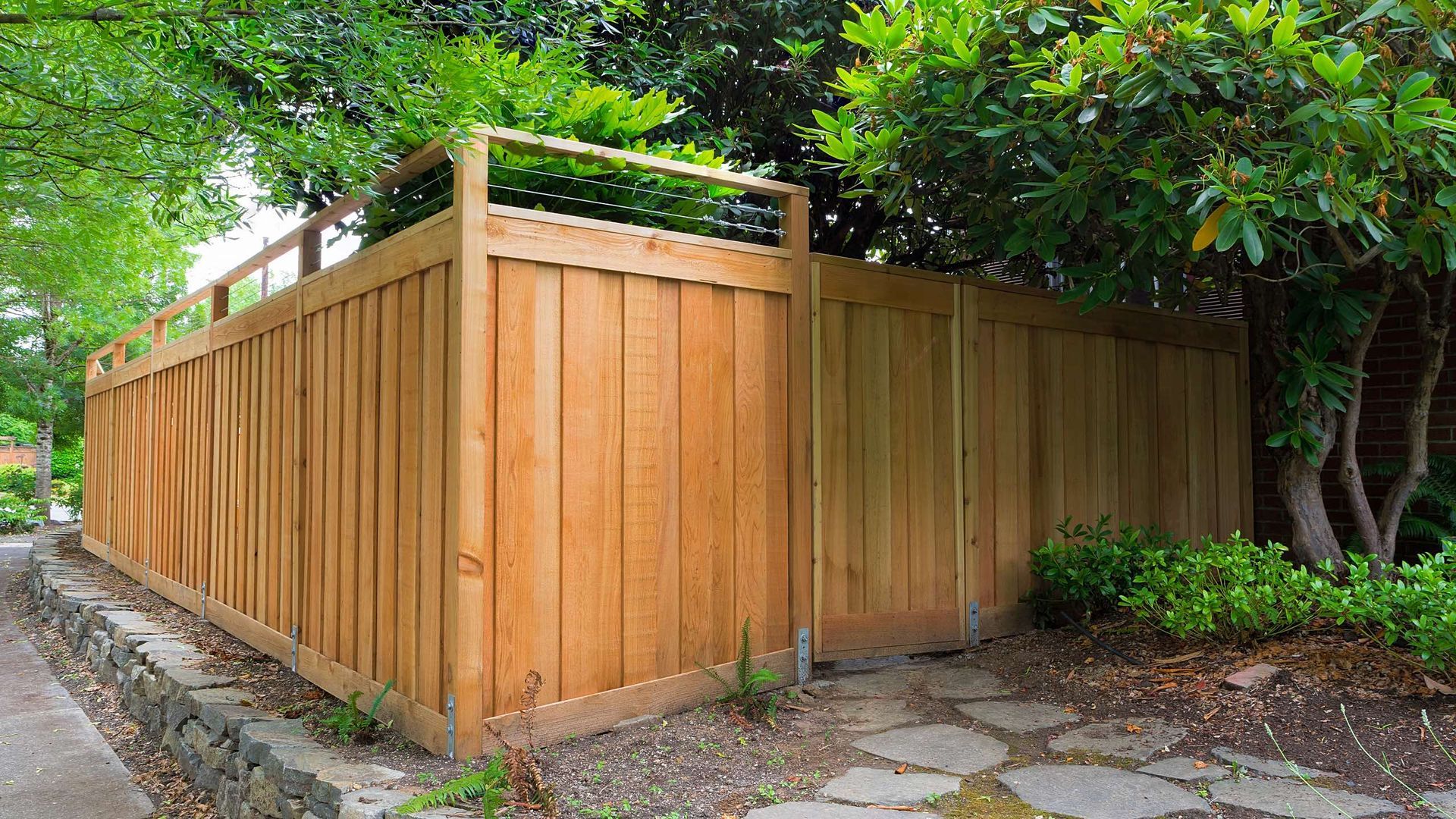 A wooden fence is surrounded by trees and a sidewalk.