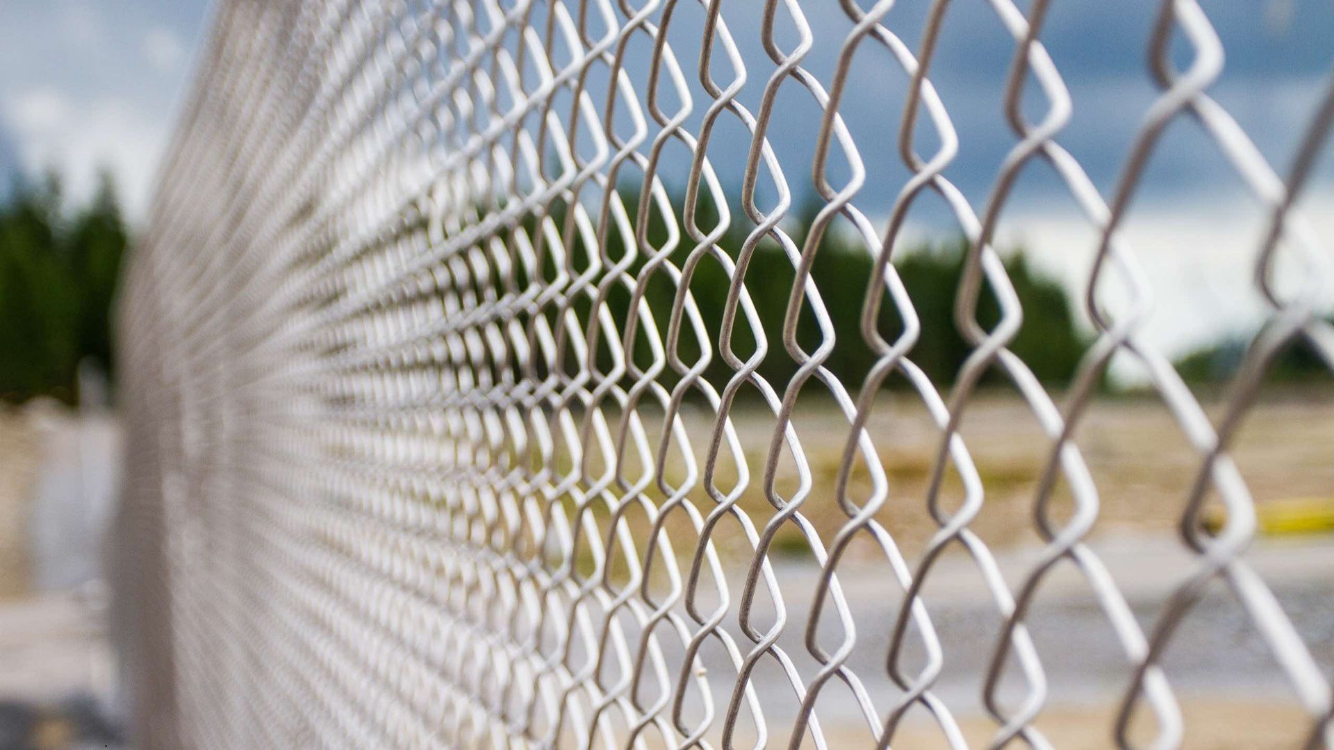 A close up of a chain link fence with trees in the background.