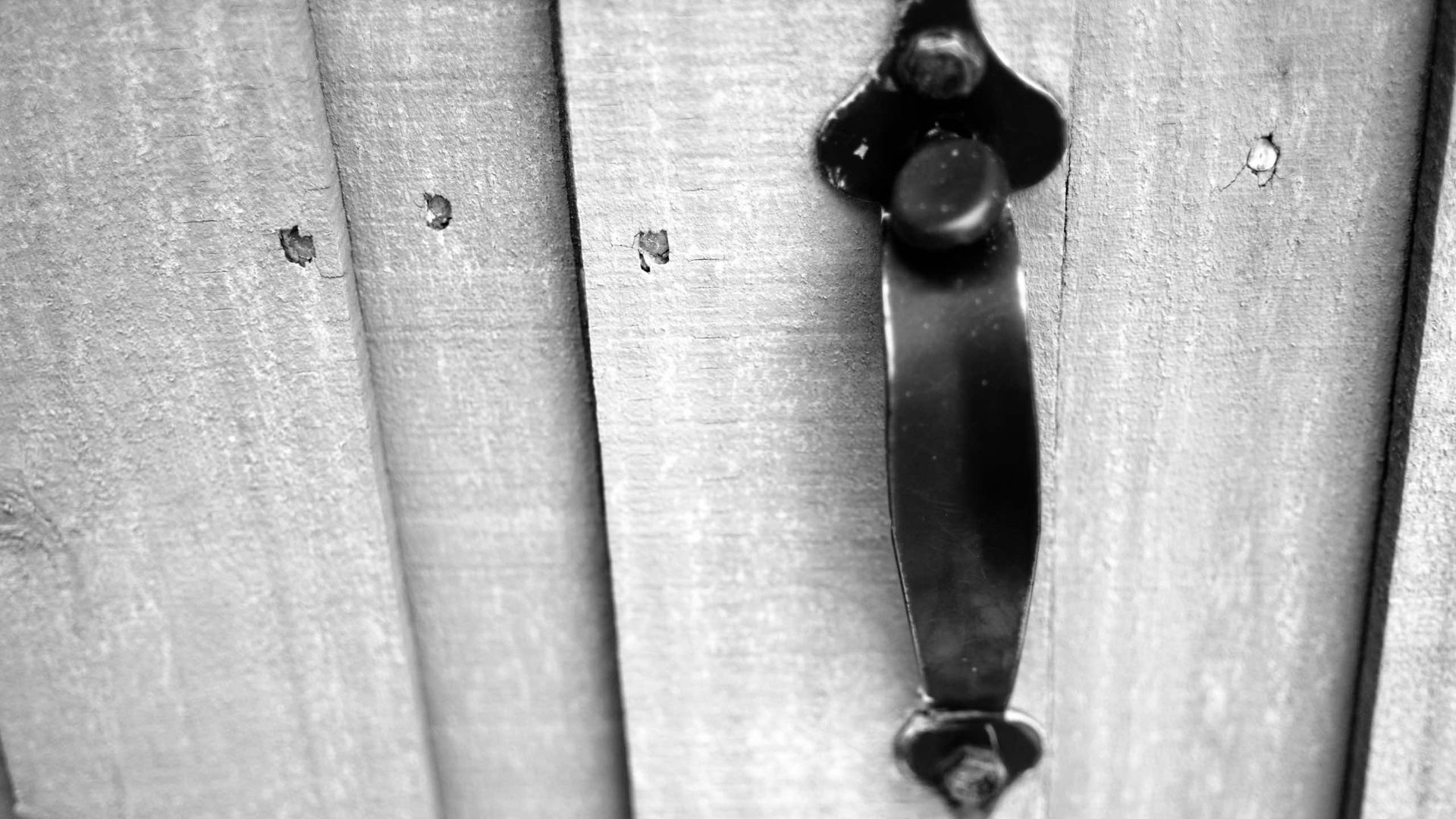 A black and white photo of a door handle on a wooden door.