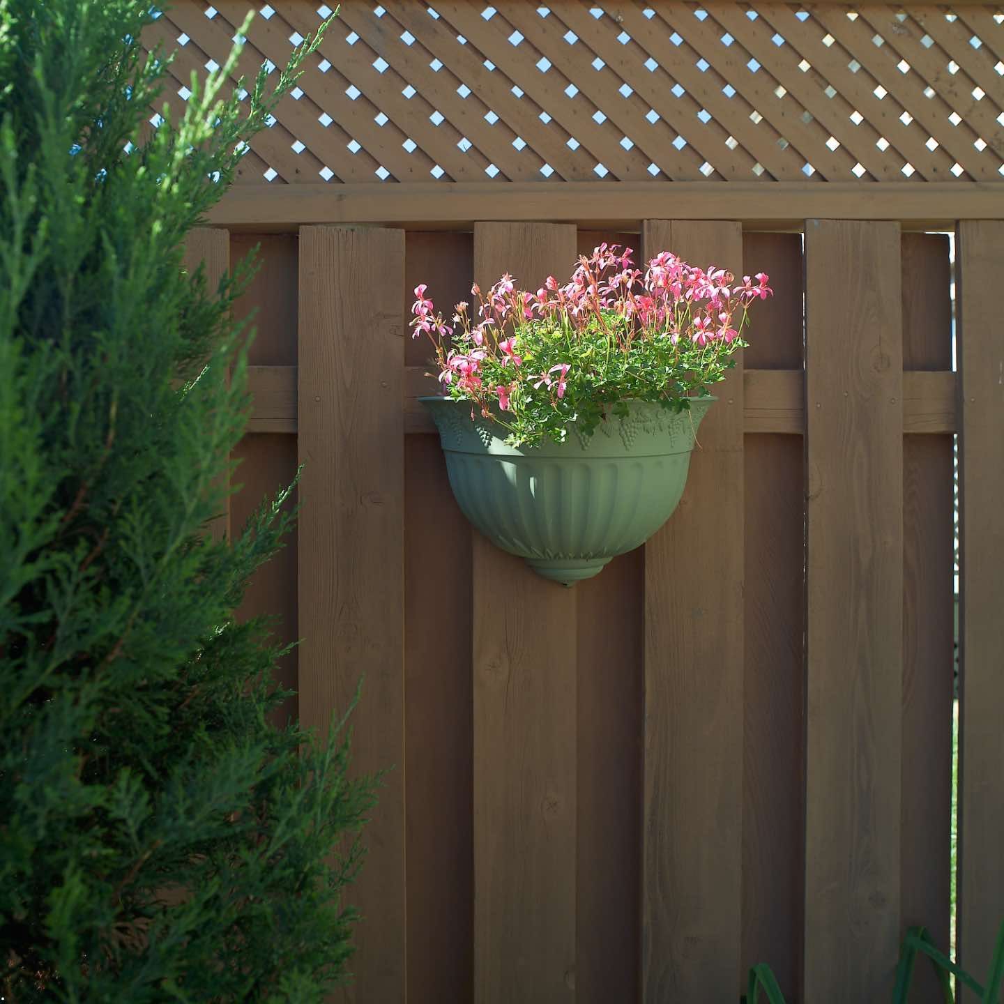 A green planter with pink flowers hanging from a wooden fence