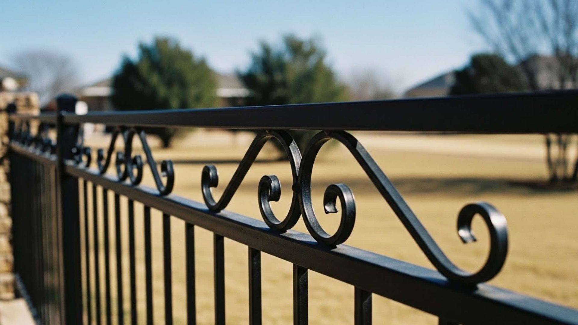 Black metal fence railing with decorative scrollwork against a blurred grassy yard.
