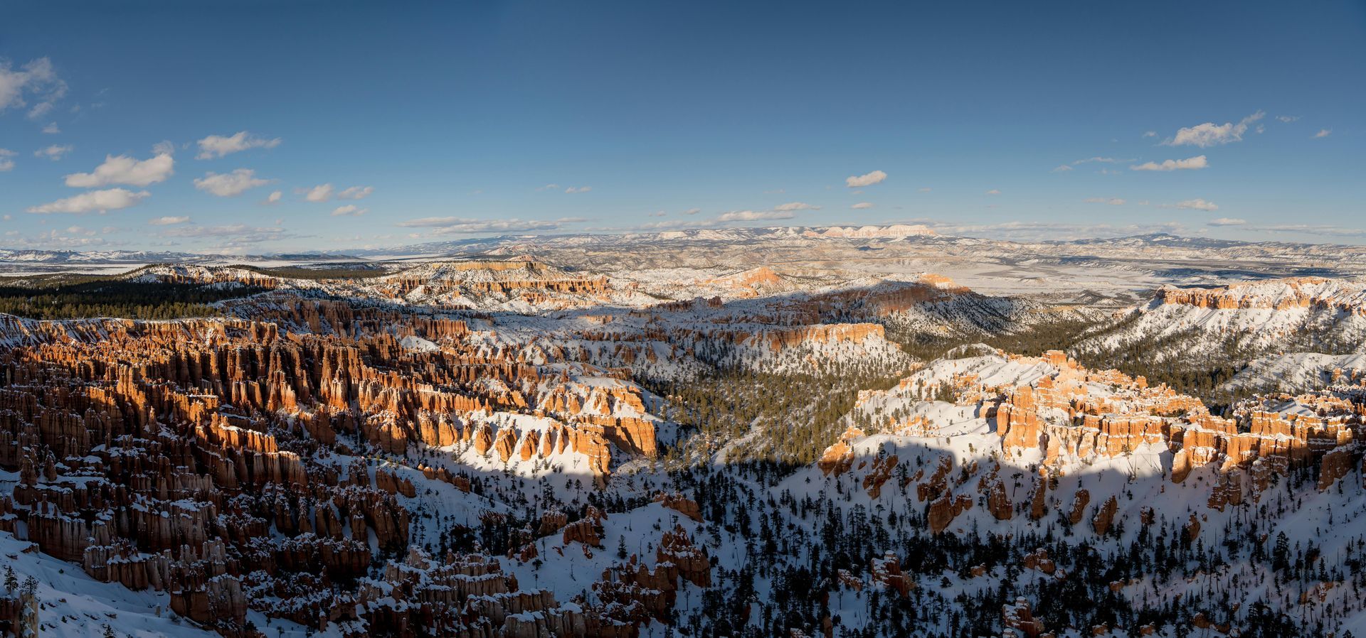 Snowy mountain valley at sunrise, with golden light on pine-covered cliffs beneath a clear blue sky