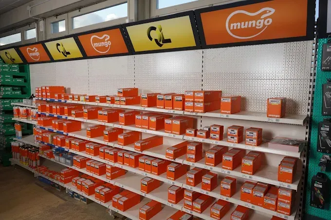Des rayons remplis de produits en boîte orange sous une enseigne de marque « Mungo » dans un magasin.