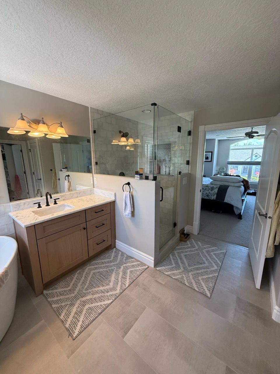 Bathroom with light wood vanity, glass shower, and open doorway to bedroom.