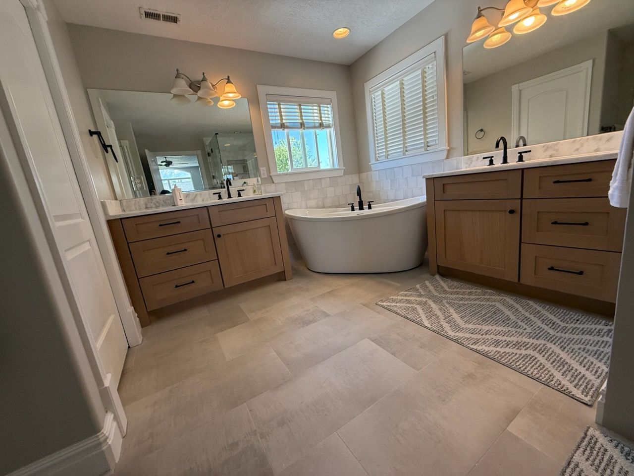 Bathroom with light wood cabinets, white bathtub, and neutral-toned flooring.